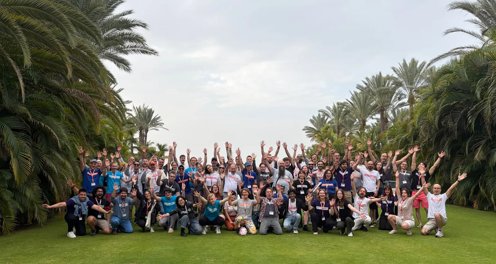 The SOFTGAMES team cheering with raised arms on a lawn between palm trees